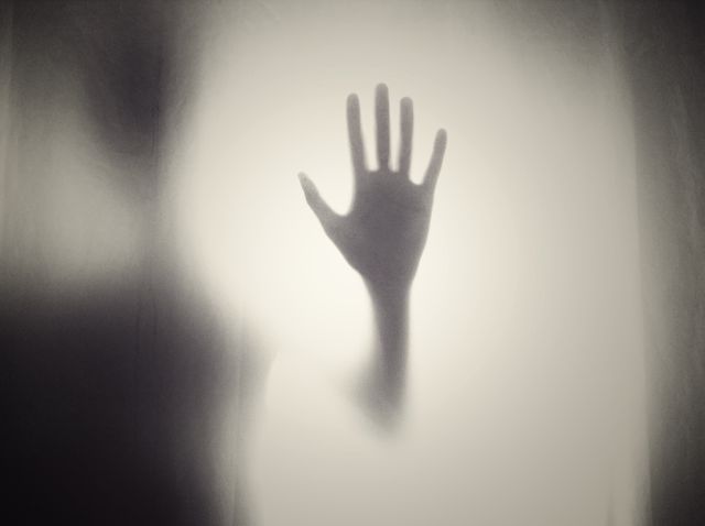 Silhouette of a hand pressed against an opaque glass, conveying a sense of mystery and spookiness. Ideal for use in horror or mystery themed projects, advertisements for thrillers, background for Halloween promotions, and artistic expressions of fear or the unknown.