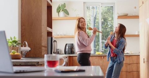 Mom and Daughter Singing with Wooden Spoons in Cozy Kitchen