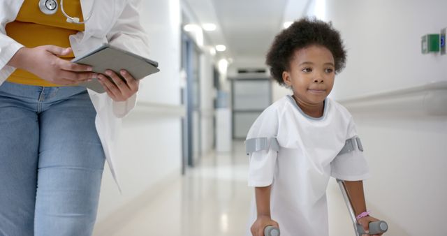 Young child using crutches in hospital corridor assisted by doctor holding a tablet - Download Free Stock Images Pikwizard.com