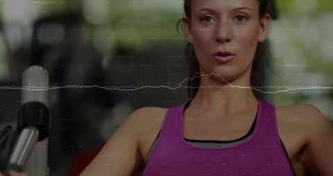 Female athlete pulling cable row handles while tracking heart rate data overlay