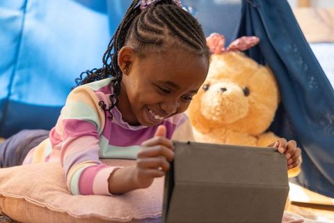 African american girl using tablet in cozy indoor tent nook with teddy bear