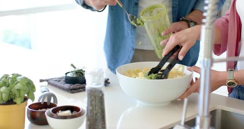 Couple mixing fresh pesto pasta in bright modern home kitchen