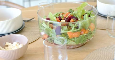 Glass salad bowl with arugula, roasted beets, sweet potato and feta on wooden dining table
