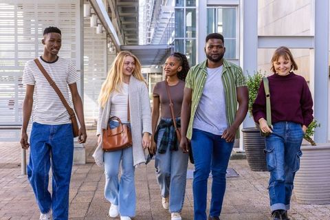 Multiracial young adults walking on campus carrying bags casual urban college friends