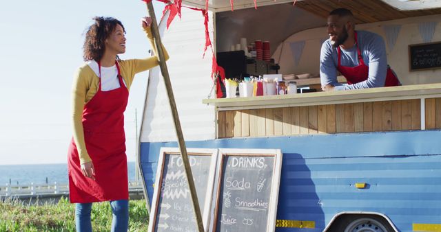 Portrait of african american couple wearing aprons smiling while standing near the food truck. food truck and street food concept