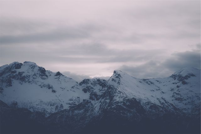 This image captures snow-covered mountain peaks during twilight, illuminated by soft light. Ideal for use in travel promotions, winter sports advertising, backgrounds for inspirational quotes, or nature-themed publications.