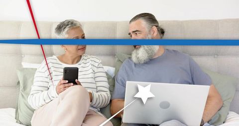 Mature couple sharing technology in cozy bedroom, browsing smartphone and laptop together