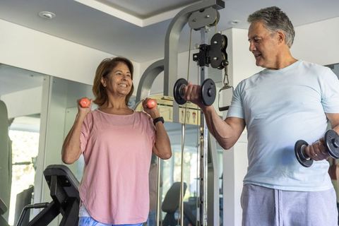 Active mature couple exercising with dumbbells in bright home gym smiling together