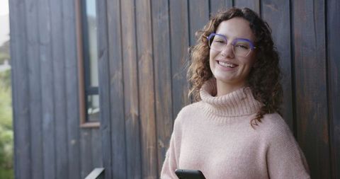 Smiling woman with smartphone leaning on wooden wall