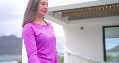 Senior woman enjoying oceanfront balcony at coastal home with hammock and mountain view