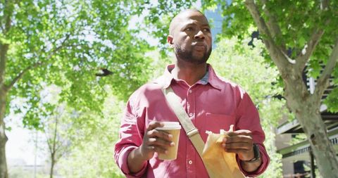 Confident Man Enjoying Lunch on Walk Under Green Trees