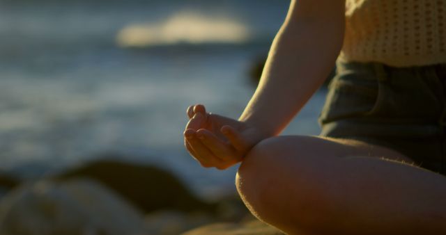 Close-up image of a person's hand and leg while meditating outdoors near a body of water. Ideal for wellness, mindfulness, and self-care content. Useful for promoting yoga classes, relaxation techniques, and stress management resources.