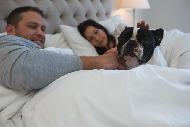 Couple petting their pet dog in bedroom at home