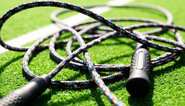 Braided colorful jump rope lying on synthetic turf with black handles and shadows