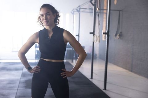 Confident athlete standing hands on hips in crossfit gym wearing black crop top and smartwatch