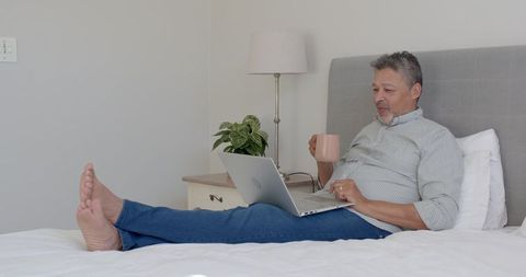 Senior Man Relaxing with Laptop and Coffee in Bright Bedroom