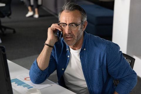 Middle-aged man talking on phone while reviewing business charts in open-plan office