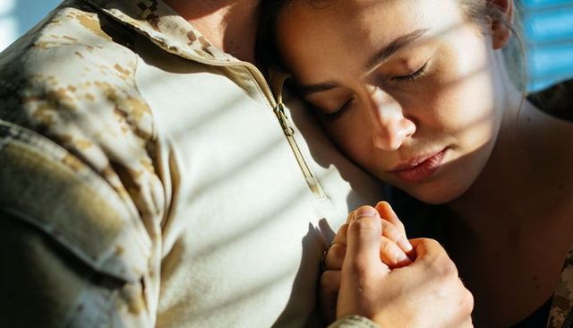 Soldier and partner holding hands in tender embrace with sunlight and blinds