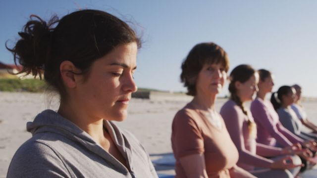 Group of women practicing yoga and meditation on a beach during sunny day with eyes closed, symbolizing relaxation and mindfulness. Ideal for promoting wellness retreats, outdoor fitness programs, and holistic health practices. Perfect for websites, blogs, and advertisements focused on healthy lifestyles and mindfulness activities.