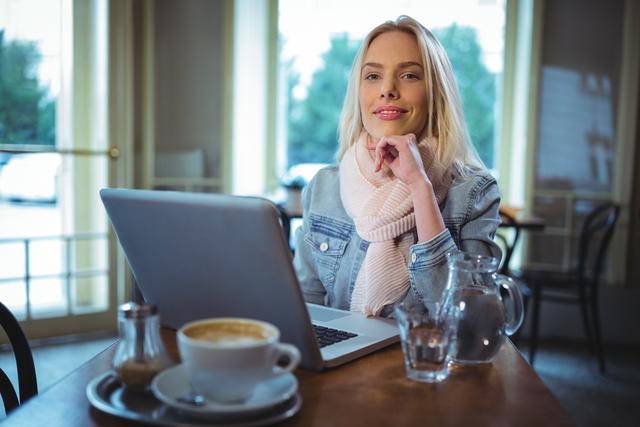 Portrait of smiling woman using laptop while having coffee in cafÃ©