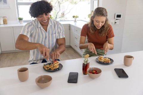 Young couple sharing pancakes and laughing at sunny modern kitchen breakfast bar