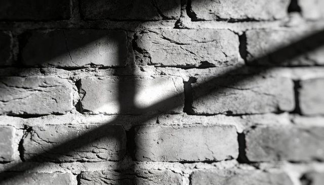 Sunlight casting cross shadow on weathered brick wall showing cracks and textured mortar