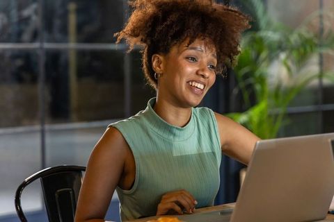 African american woman smiling and working on laptop in modern coworking space in mint top