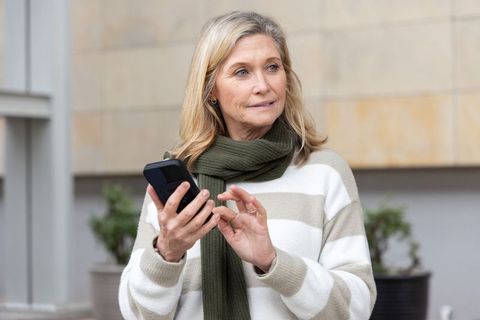 Mature woman using smartphone in urban plaza wearing striped sweater and green scarf