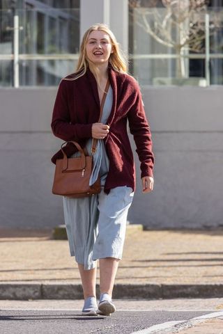 Young woman walking on urban sidewalk in burgundy cardigan carrying brown leather bag