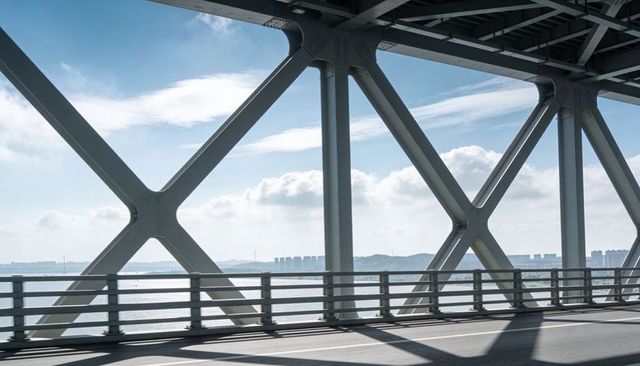 Industrial Steel Truss Bridge Casting Geometric Shadows Over Coastal Roadway Skyline