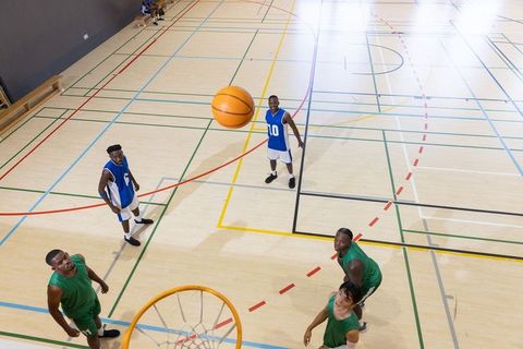 Diverse male basketball players jumping for rebound on indoor hardwood court during game
