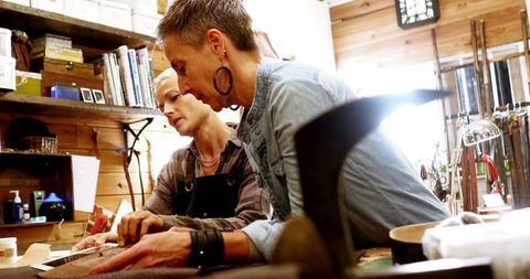 Craftswomen Skillfully Crafting Leather Covers in Rustic Workshop