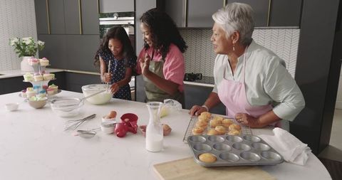 Multigenerational family baking colorful cupcakes together in bright modern kitchen