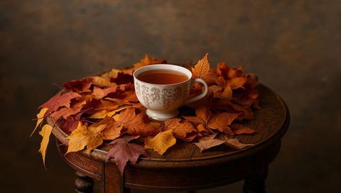 Filigree porcelain teacup resting on autumn maple leaves on vintage wooden table