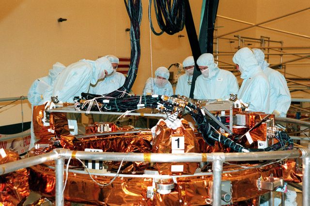This image captures astronauts engaged in a detailed examination of the Flight Support System (FSS) while preparing for the repair and upgrade mission of the Hubble Space Telescope during a Crew Equipment Interface Test. The image shows a focus on said equipment critical for mission activities. Great for illustrating precision work in aerospace engineering and showcasing team collaboration in high-stakes environments.