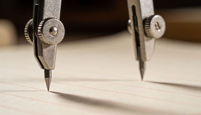 Macro steel drafting compass measuring precision on ruled paper close-up for design