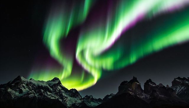 Dancing northern lights swirling over snow-covered mountain peaks under starry night