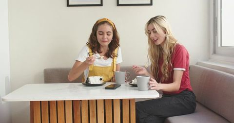 Friends sharing cake in sunlit dining nook, cozy conversation and coffee mugs
