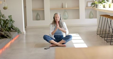 Mature Woman Meditating in Sunlit Modern Space with Greenery