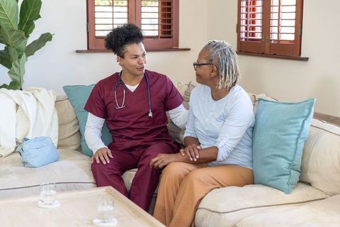 Young male caregiver reassuring senior african american woman during home care visit