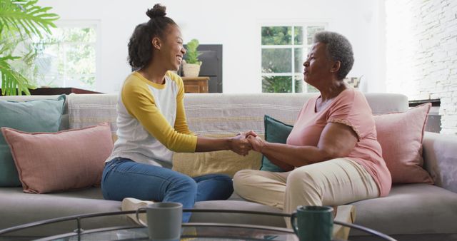 African american mother and daughter holding hands and smiling sitting on the couch at home. motherhood and love concept
