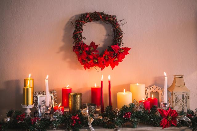 Christmas candles and decorations creating a warm, festive atmosphere on a fireplace mantle. Red and white candles, poinsettias, and a wreath add to the holiday cheer. Perfect for illustrating holiday decor, festive greetings, seasonal advertisements, and home interior inspiration.