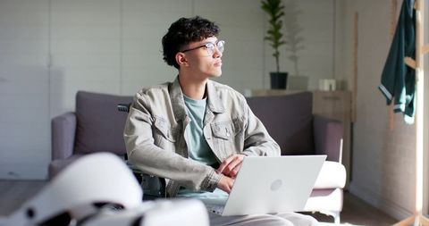 Asian man in wheelchair using laptop working remotely and embracing independent living