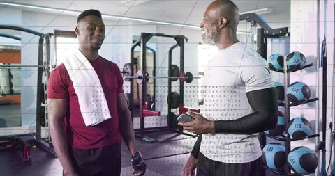 Gym trainer coaching client reviewing workout plan on smartphone during strength session