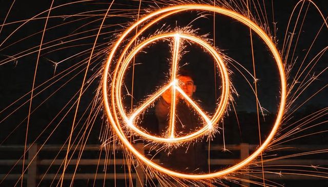 Long exposure light painting peace symbol using sparkler circle around man at night