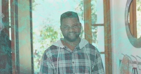 Smiling man standing in sunlit entryway wearing plaid hoodie with teal overlay