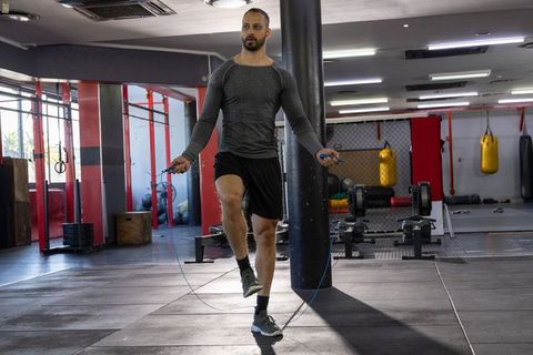 Indian man jumping rope for cardio in commercial gym wearing long-sleeve top and shorts