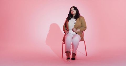 Fashionable woman on chair with pink backdrop in studio
