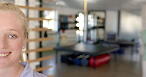 Smiling woman standing by wooden wall bars in physiotherapy clinic with exercise equipment