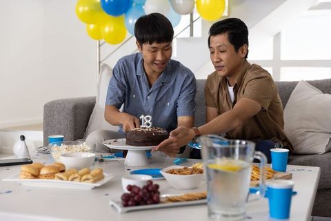 Asian men celebrating 18th birthday at home with chocolate cake, balloons, snacks